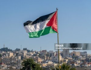 "A large Palestinian flag waves proudly above the city of Jerusalem, symbolizing hope, resistance, and the enduring spirit of the Palestinian people. The ancient city's iconic structures, including the Dome of the Rock, can be seen in the background under a vibrant sky."