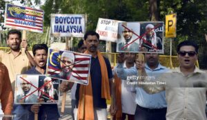 Protesters holding Dr. Zakir Naik's picture with a 'Boycott' sign in the background."